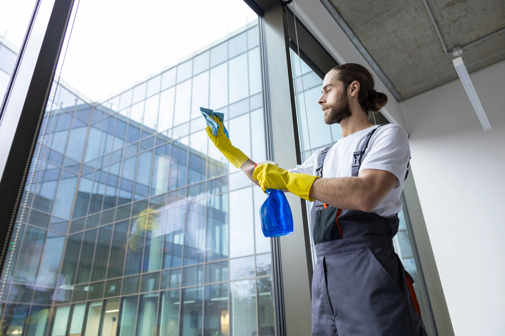 Professionelle Gebäudereinigung – Reinigungskraft reinigt große Glasfassade eines Gebäudes.